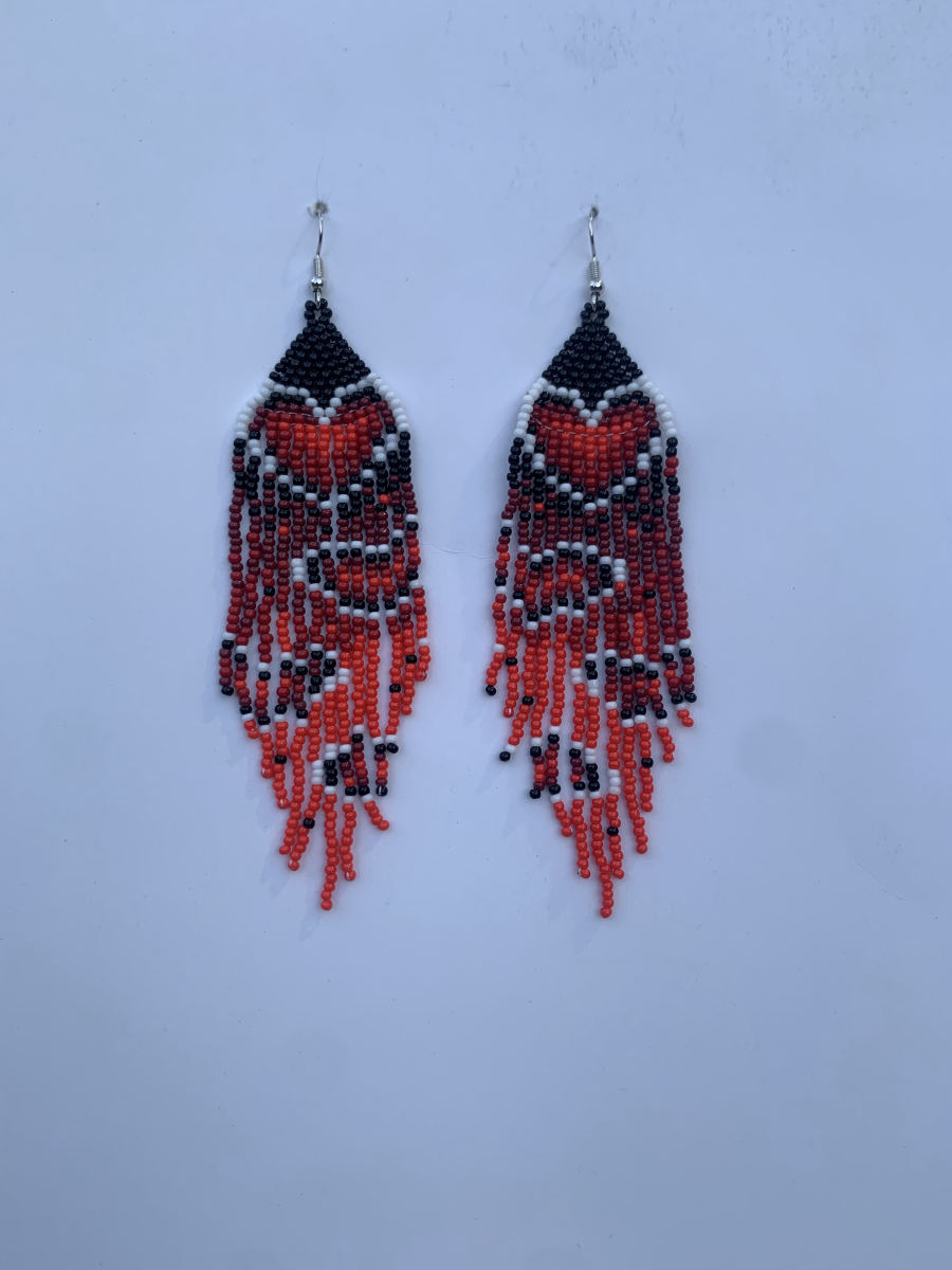 Long fringe earrings with bold orange-red and white geometric chevron stripes through a black body, staggered strand ends, wire hook.