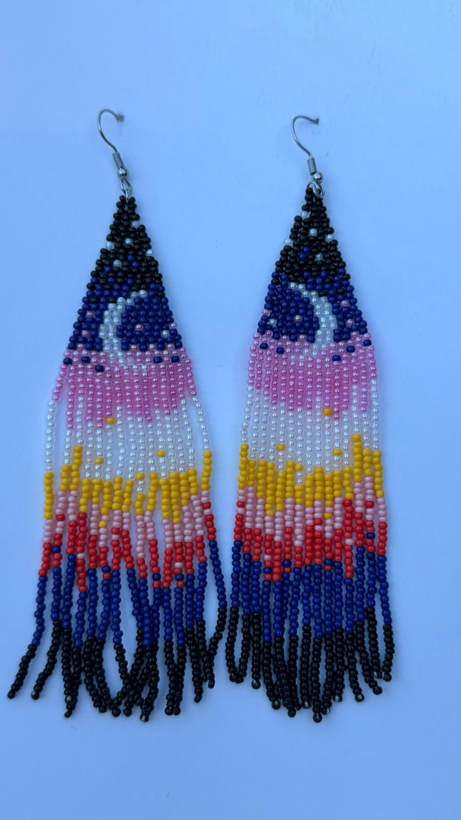 Long triangular drop earrings with rainbow waterfall fringe in cobalt blue, bubblegum pink, white, golden yellow, coral red, and black seed beads with silver fish-hook closures.