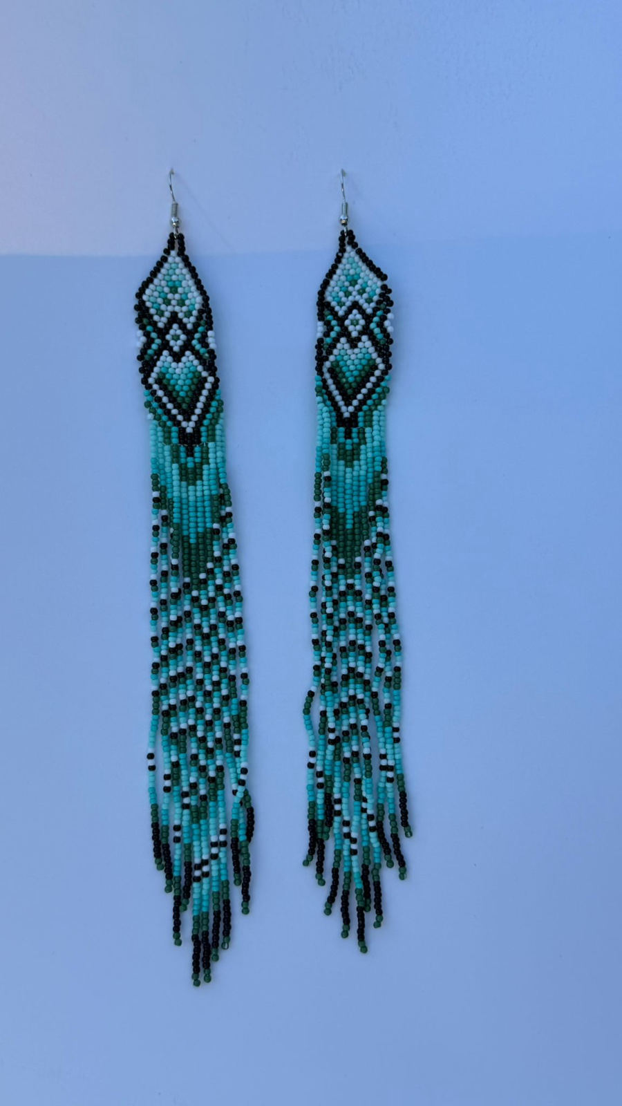 Very long fringe drop earrings with nested diamond geometric header panel in black, white, aqua turquoise, and forest green seed beads, extra-long fringe continuing the four-color chevron zigzag pattern the full length, silver fish-hook closures.